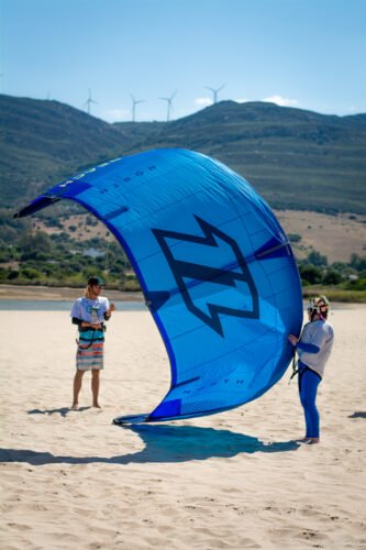 Lección de kitesurf en Tarifa, mostrando a un instructor con un estudiante en la playa.
