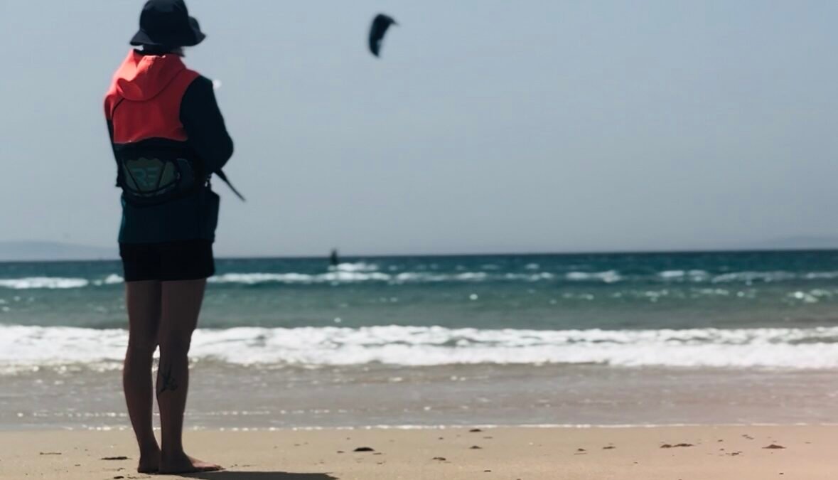 A kitesurfer riding confidently in the deep blue waters of the Atlantic Ocean in Tarifa, fully equipped with a wetsuit, harness, and safety gear, being supported by a kite.